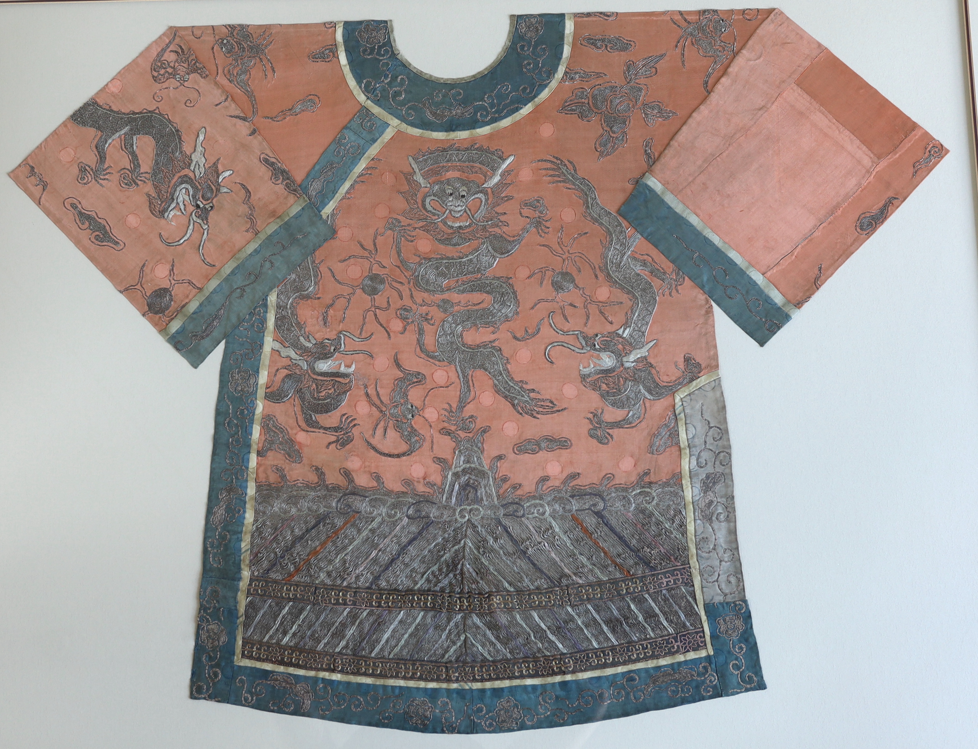 A late 19th century Chinese coral silk and silver metallic embroidered dragon robe, the dragons surrounded by auspicious embroidered symbols. The robe, split into back and front panels, separately framed within a deep do